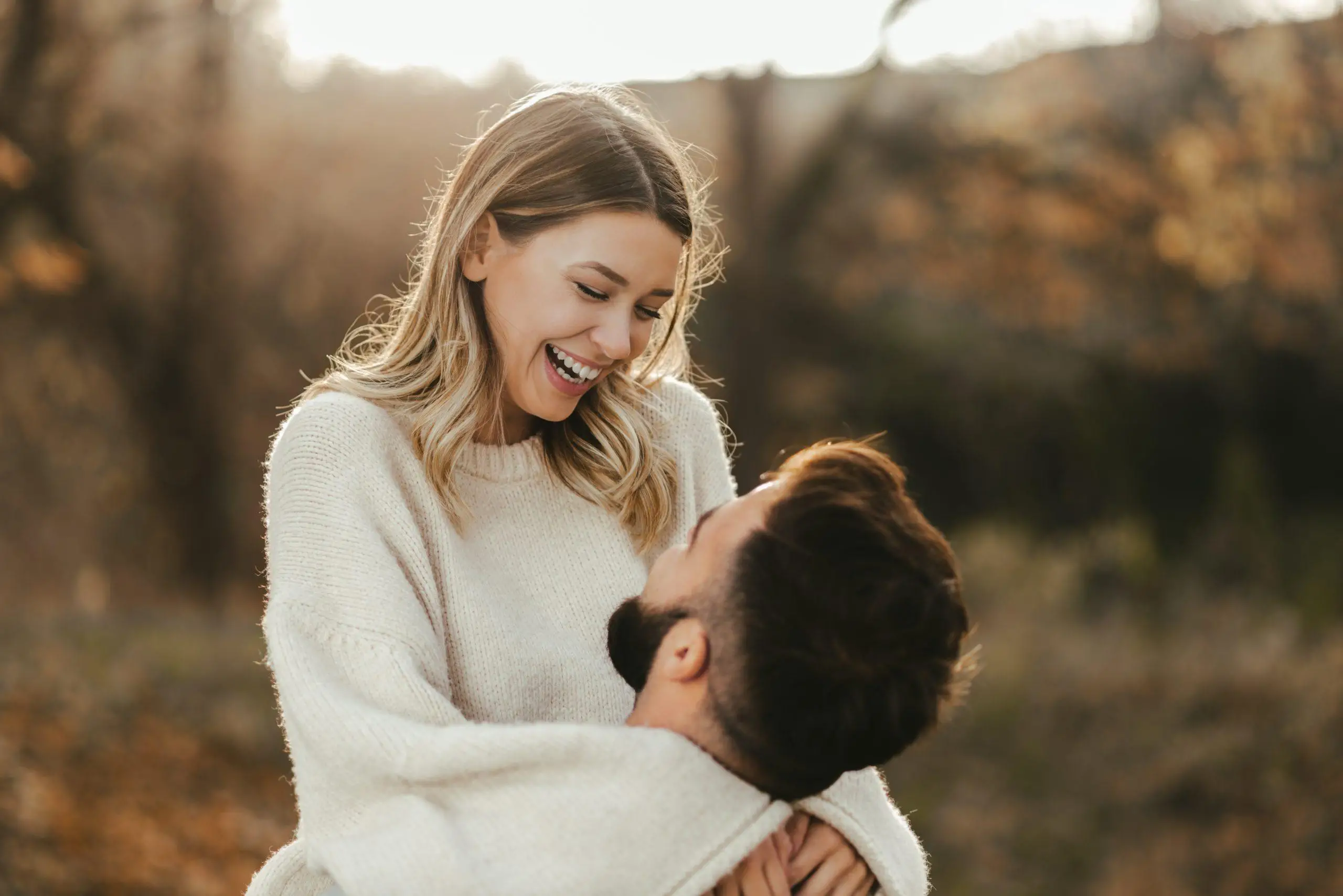 Young cheerful couple having fun in nature during autumn. Woman being carried by her boyfriend